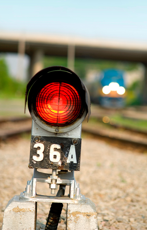 Red safety warning light beside train railway tracks.